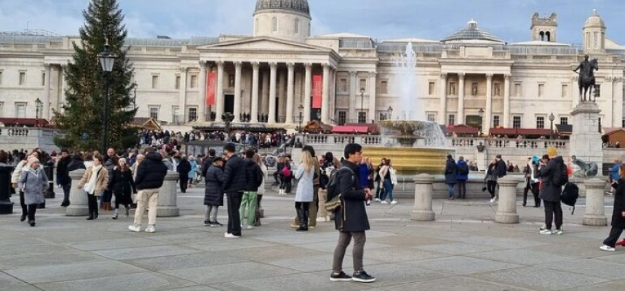 Crowded Trafalgar Square in London with people walking and gathering near the fountain and Christmas tree, National Gallery in the background. London Harry Potter Filming Locations Tour.