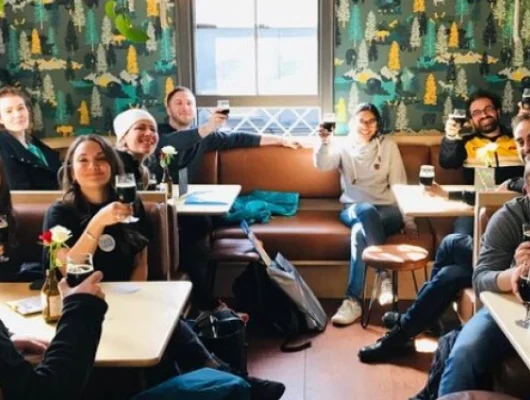 Group of people enjoying drinks and socializing in a cozy cafe with colorful wallpaper and natural light at Brighton Independent Foodies Tour