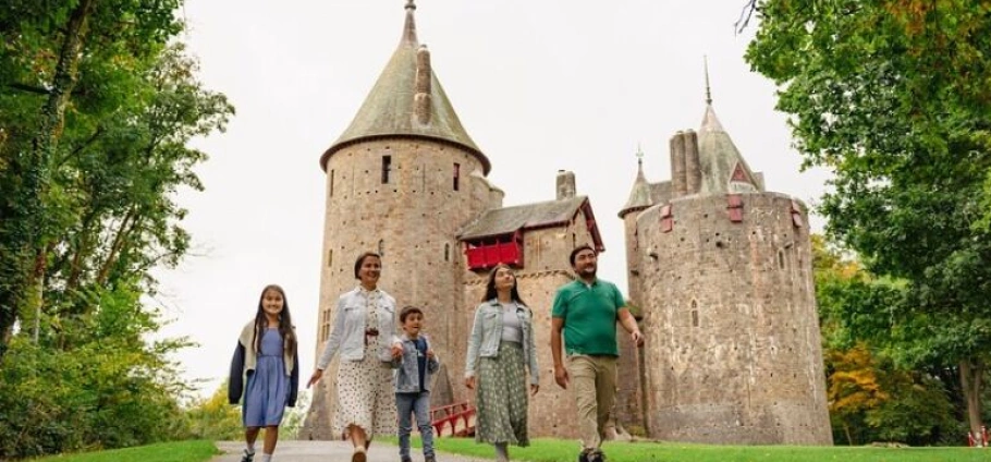 Cardiff Castles Guided Sightseeing Tour | Family walking in front of a historic stone castle surrounded by lush greenery.