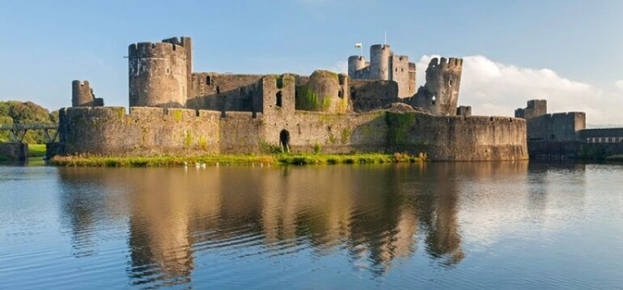 Cardiff Castles Guided Sightseeing Tour | Medieval castle with reflection on a calm lake under a clear blue sky.