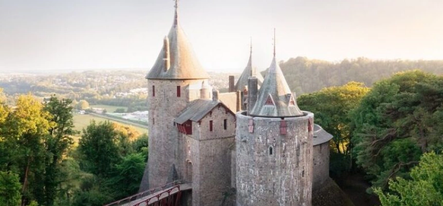 Cardiff Castles Guided Sightseeing Tour | Medieval stone castle with tall towers surrounded by lush green forest and distant hills.