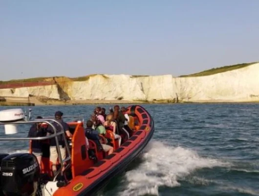 Brighton RIB Ride & Lighthouse Tour || Tourists on a red speedboat enjoying a ride near white cliffs by the sea on a sunny day.