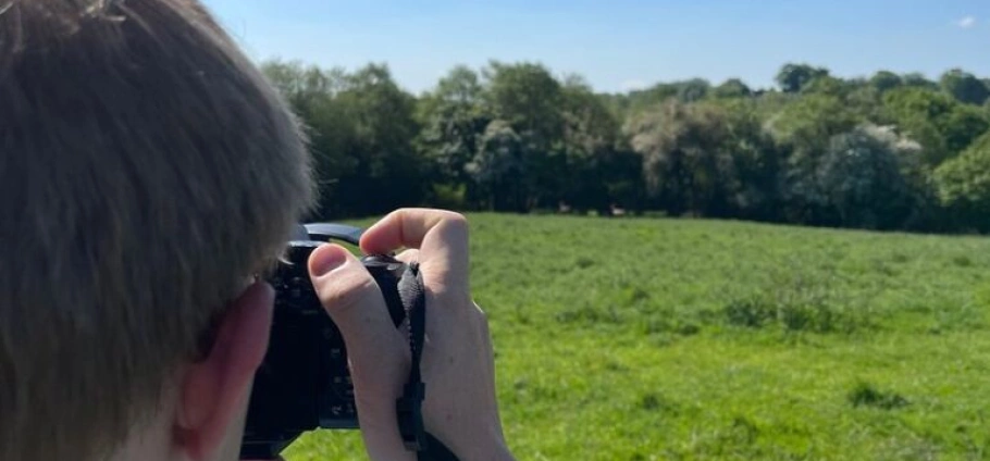 Staffordshire Deer Park Photography Tour | Person holding a camera and photographing a field with trees in the background on a sunny day.