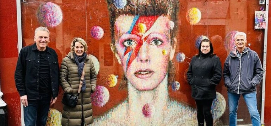 150 Minute David Bowie Trivia Tour | Four people standing in front of a colorful mural featuring a famous musician with a lightning bolt face paint.