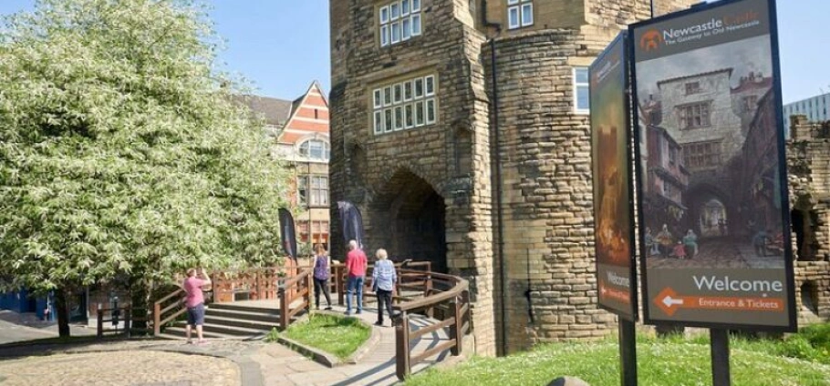 Newcastle Castle | People walking toward the entrance of Newcastle Castle, with a welcome sign and a large tree to the left.