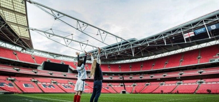 Two people celebrating on the field at the Wembley Stadium Tour with empty red seats in the background