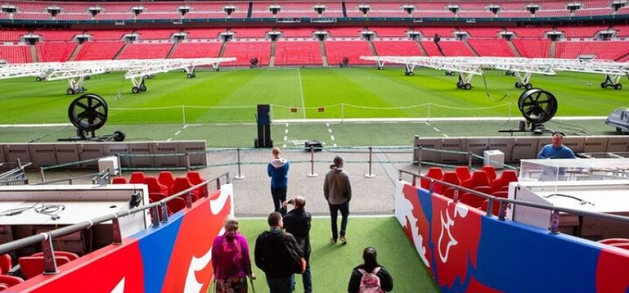 Visitors on the Wembley Stadium Tour, touring an empty stadium with green field and red seats