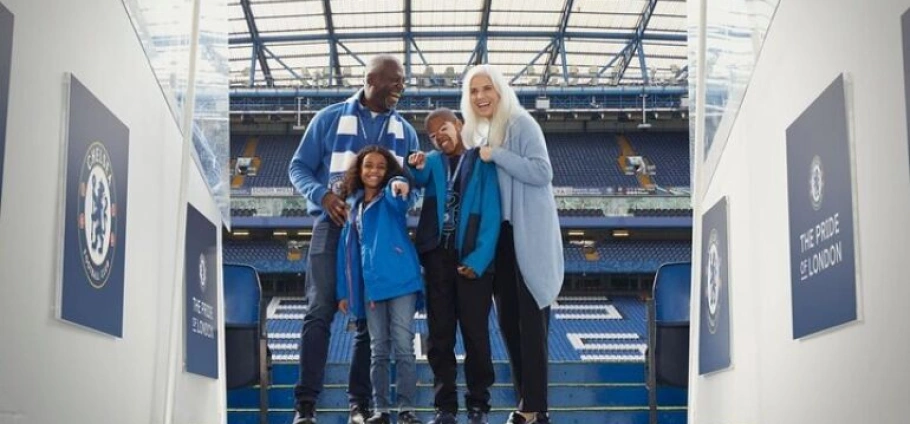 Family wearing Chelsea FC gear smiling on the London Chelsea FC Stadium Tour