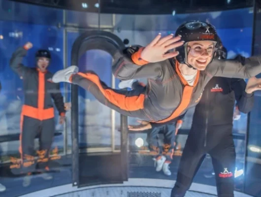 Indoor skydiving experience with participants in flight suits and helmets inside a wind tunnel.