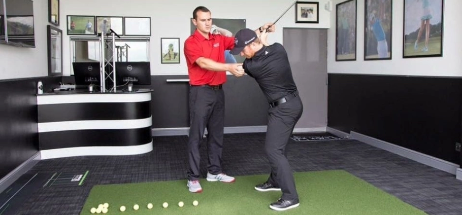 PGA Professional 30 Minute Golf Lesson | Golf instructor teaching a student proper swing technique in an indoor training facility.