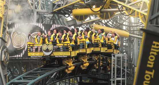 People riding a yellow and black roller coaster at Alton Towers theme park.