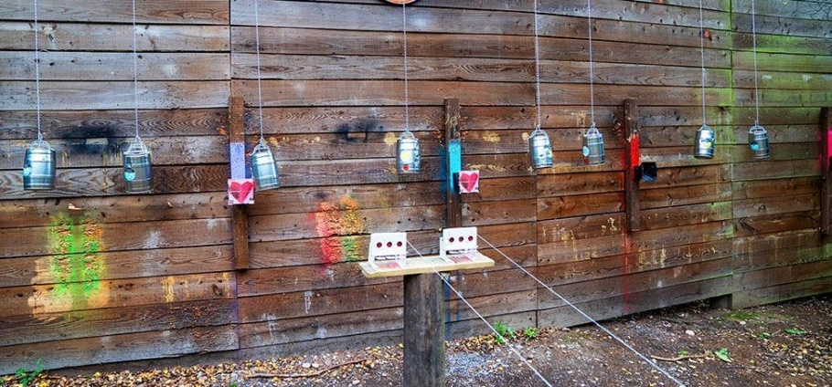 Rifle Shooting Experience Birmingham target practice area with hanging metal cans and colorful paint splatters on a wooden wall.