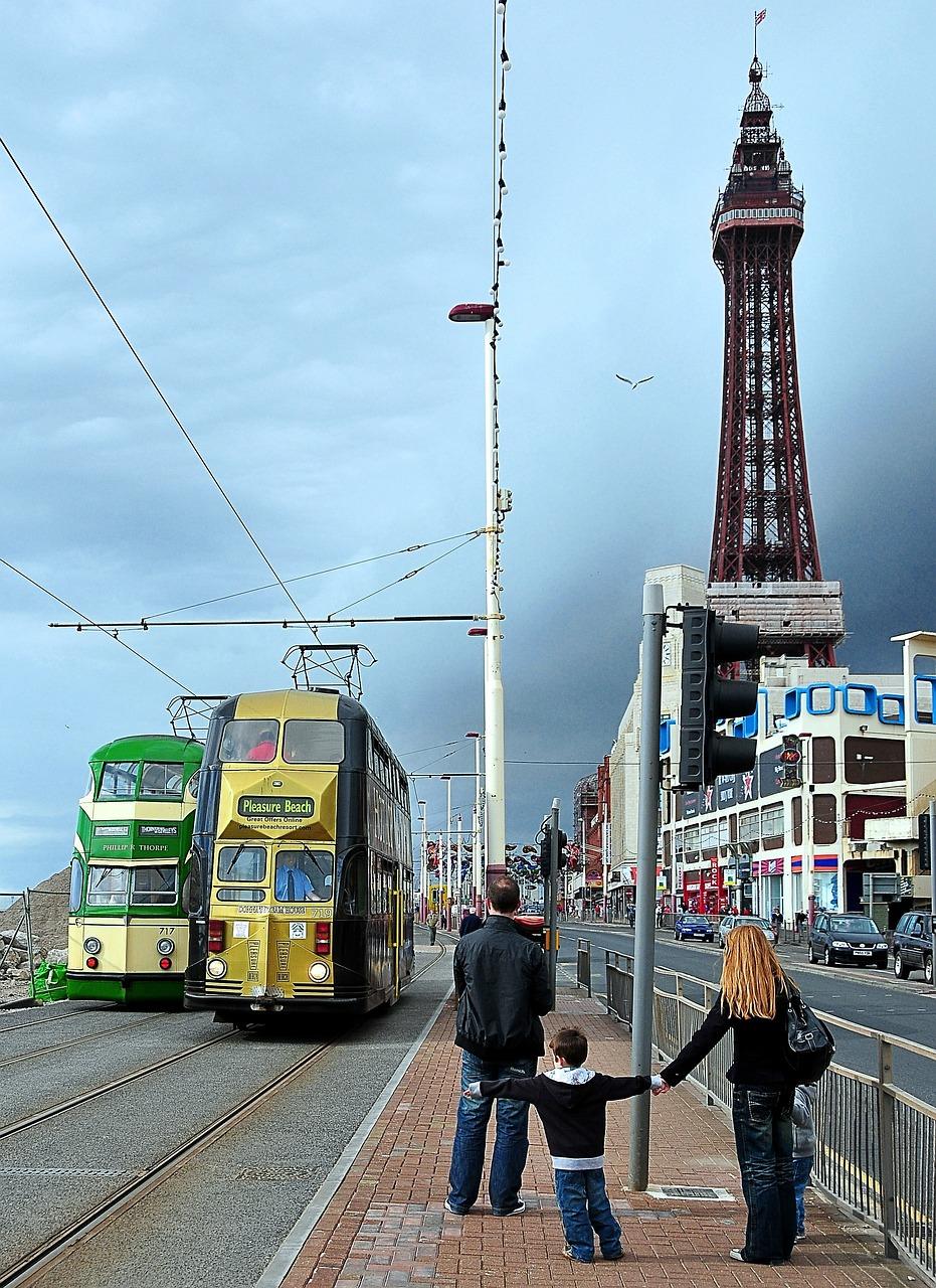 A family standing on a pavement observing a double-decker tram, with the Blackpool Tower visible in the background.