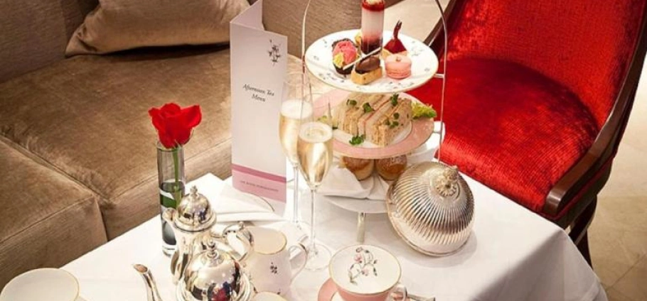 Buckingham Palace with Afternoon Tea for Two | Elegant afternoon tea setup with a tiered tray of pastries and sandwiches, a rose in a vase, and a menu on a white tablecloth.