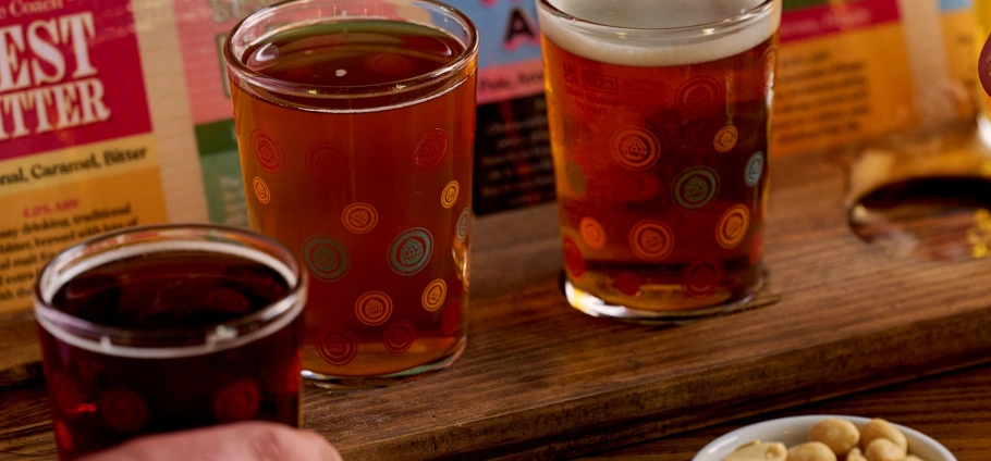 Craft Beer Experience: Three glasses of craft beer on a wooden tray with a bowl of nuts in the foreground.