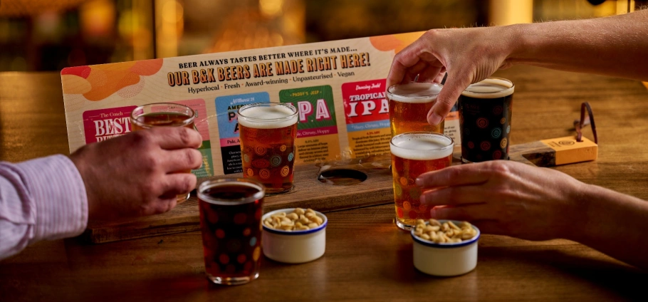 Craft Beer Experience: People enjoying a beer tasting flight with various craft beers and small bowls of snacks on a wooden table.