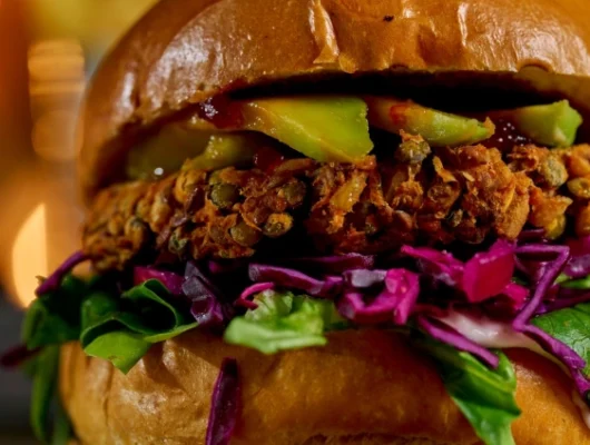 Craft Beer Experience: Close-up of a gourmet veggie burger with fresh lettuce, red cabbage, avocado, and a crispy plant-based patty in a toasted bun.