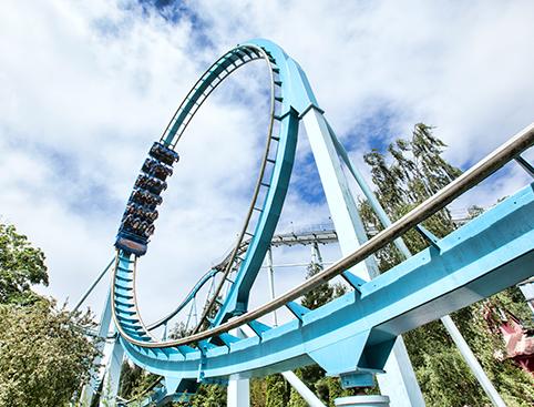 Roller coaster with a blue track and large loop against a partly cloudy sky.