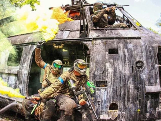 Paintball players in tactical gear exiting a damaged helicopter with yellow smoke grenades in a forest setting at Group Paintball Experience Birmingham