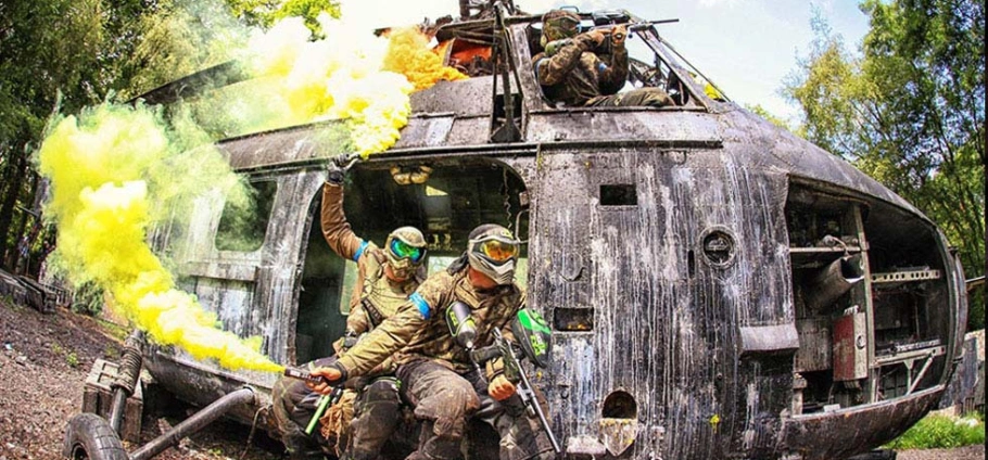 Paintball players in tactical gear exiting a damaged helicopter with yellow smoke grenades in a forest setting at Group Paintball Experience Birmingham