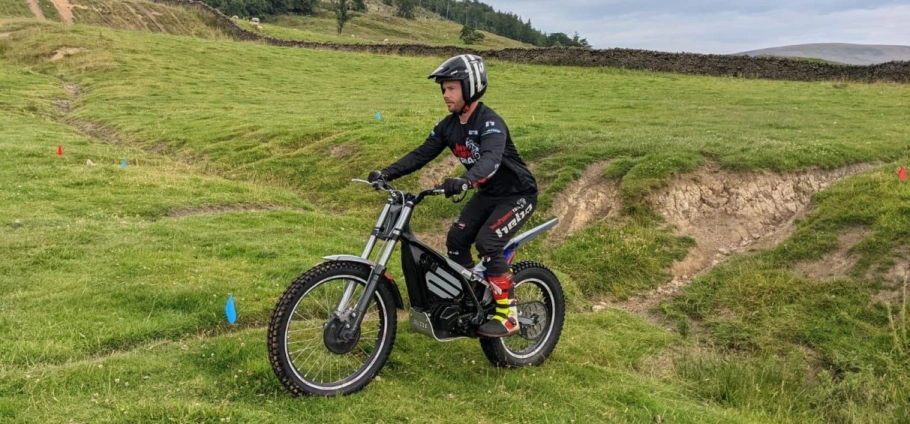 A person in motocross gear riding a trial bike on a grassy terrain.