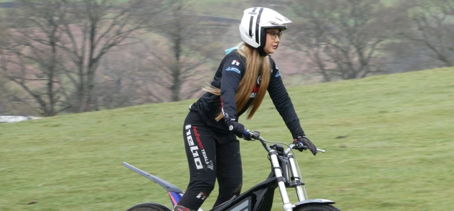 Person riding an electric mountain bike on a grassy field wearing a helmet and protective gear.