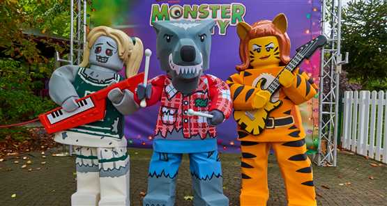 LEGOLAND Windsor Resort | Three LEGO monster figures dressed in Halloween costumes, holding musical instruments, standing in front of a "Monster Party" sign.