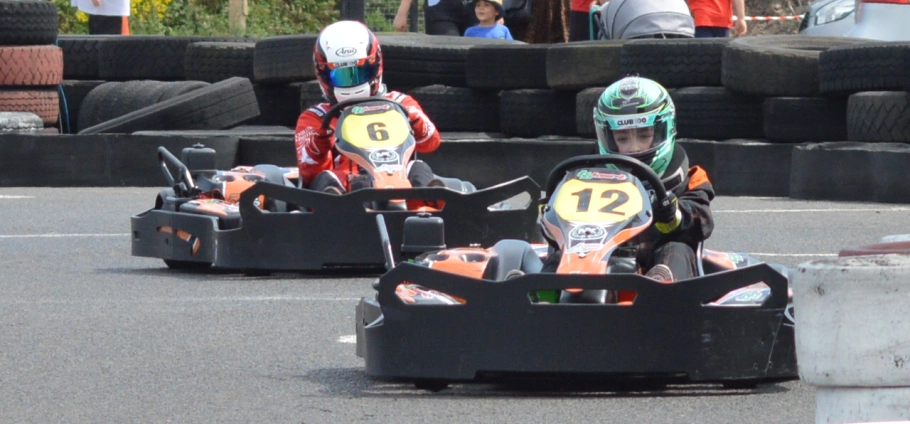 Two go-kart racers competing on a track with tire barriers in the background at Lichfield Go Kart Driving