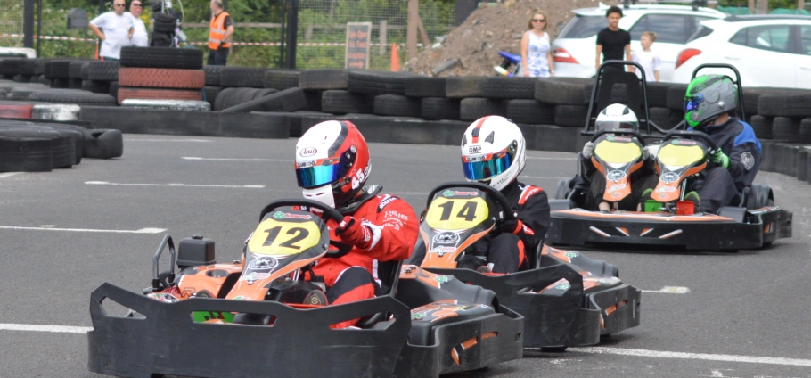 Go-kart racers competing on an outdoor track with spectators in the background at Lichfield Go Kart Driving