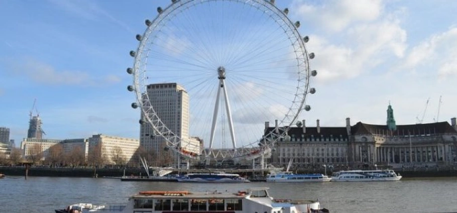 Half Day London Eye and Tower of London Tour | London Eye Ferris wheel on the South Bank of the River Thames with surrounding buildings and boats on the water.