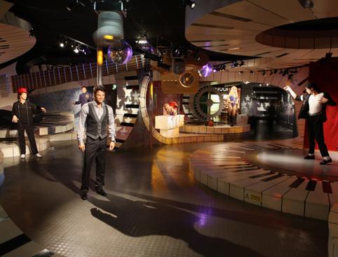 Wax figures of people in musical poses inside a themed museum exhibit with large piano keys and vibrant lighting.