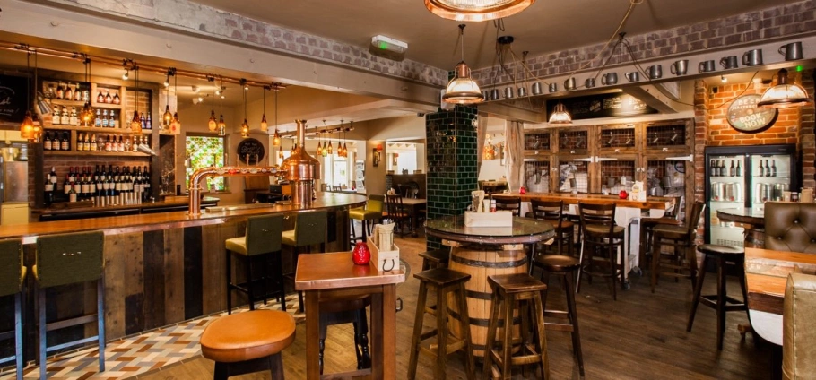 Cozy pub interior with wooden bar counter, stools, tables, and warm lighting.