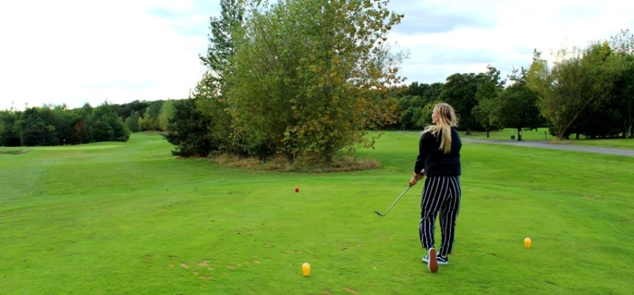 PGA Professional 30 Minute Golf Lesson | Woman playing golf on a lush green course with trees in the background