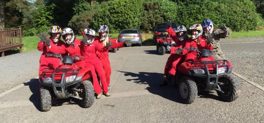 Northumberland Quad Bike Trek | Group of people in red jumpsuits and helmets posing with two quad bikes on a sunny day