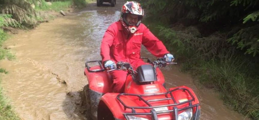 Northumberland Quad Bike Trek | Person riding a red ATV through a muddy trail in a forest.