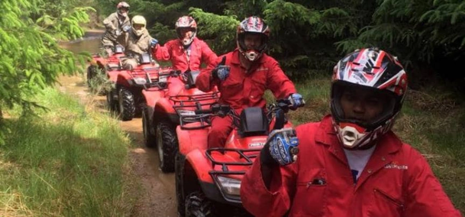 Northumberland Quad Bike Trek | Group of people riding red ATVs through a forest trail, wearing helmets and red jumpsuits.