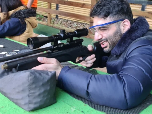 Man aiming rifle at rifle shooting Birmingham with safety glasses and winter jacket.