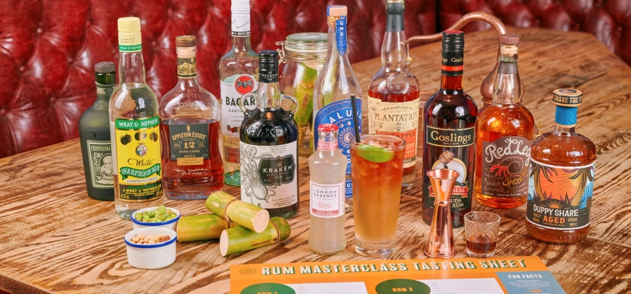 Assorted rum bottles and cocktail ingredients on a wooden table for a rum masterclass tasting session.