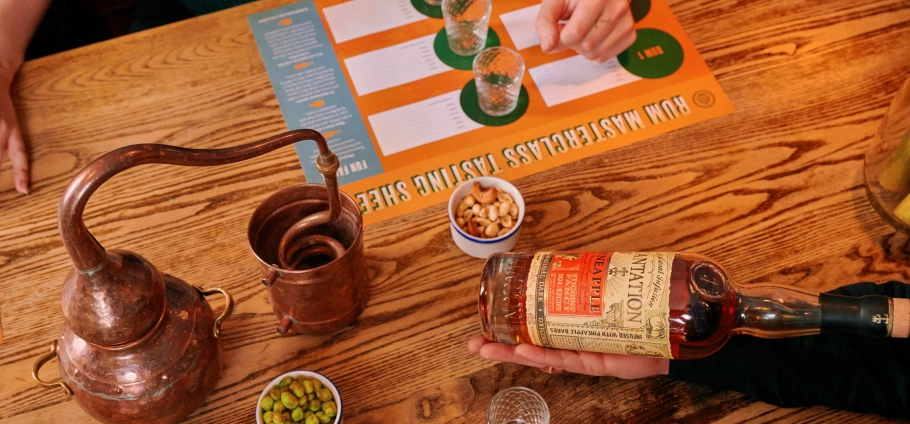 Whiskey tasting session with a copper still, tasting sheet, and snacks on a wooden table.