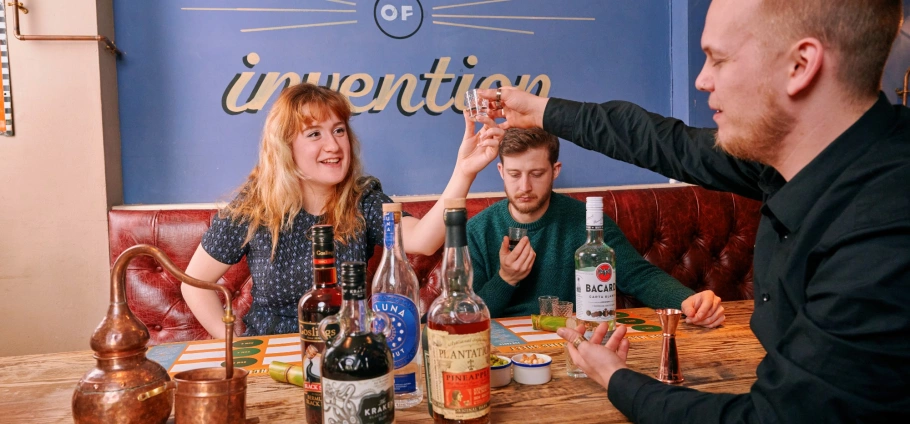 Three friends enjoying drinks at a bar with various liquor bottles on the table.