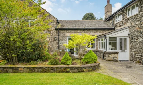 Stone house with garden and patio areas, surrounded by green bushes and trees.