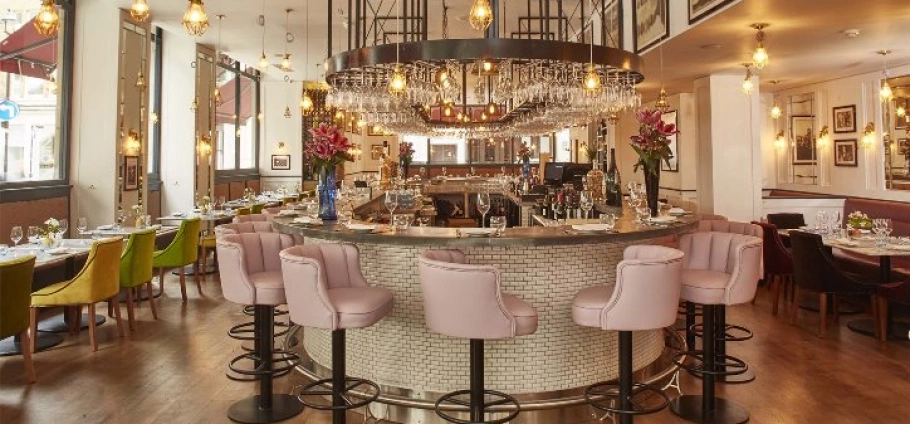 Elegant restaurant interior with a central bar, pink bar stools, hanging wine glasses, and cozy dining tables with colorful chairs. SEA LIFE London 