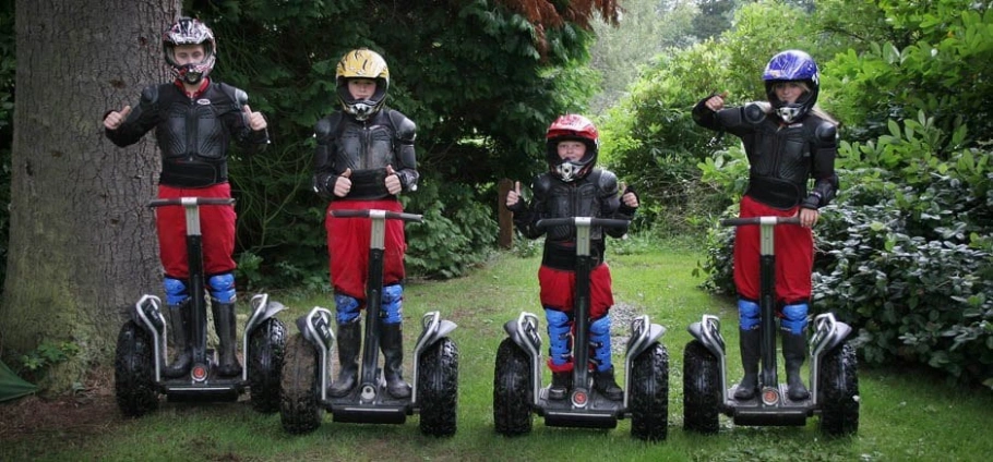 Northumberland Segway Safari | Four people wearing helmets and protective gear riding Segways in a lush green garden.