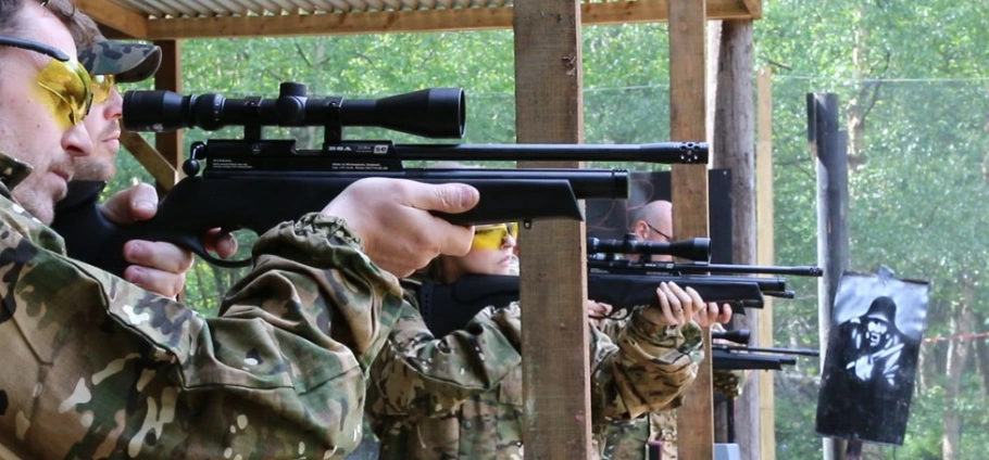 People in camouflage gear aiming rifles at a shooting range with target in the background.