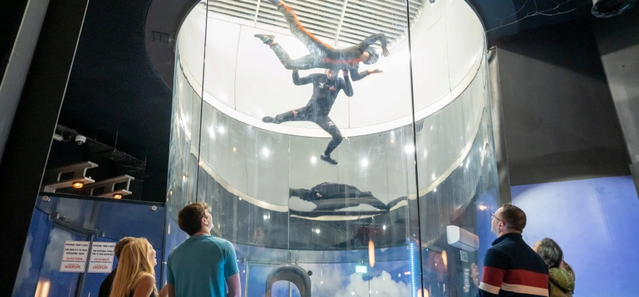 Indoor skydiving experience with spectators watching through a glass wind tunnel.