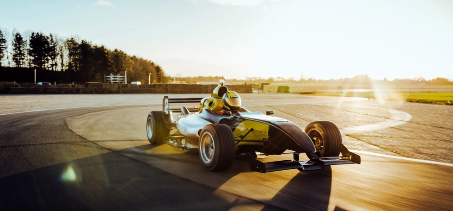 Ultimate Motorsports Race Day Experience in London | Race car driver maneuvering a sleek black and yellow formula car on a sunny racetrack curve.