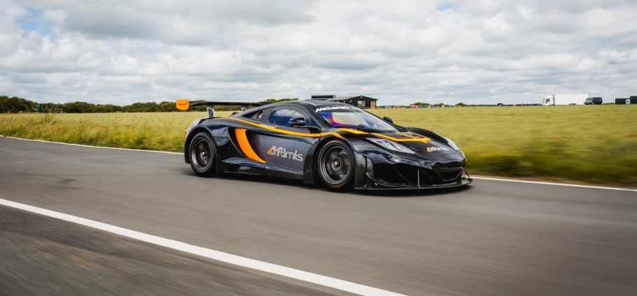 Ultimate Motorsports Race Day Experience in London | High-performance sports car driving on a countryside road with green fields and cloudy sky in the background.