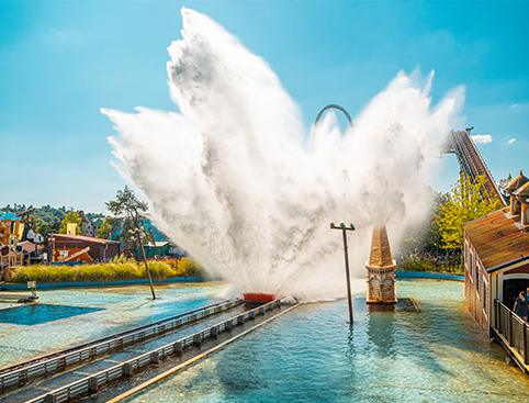 THORPE PARK Resort | Water ride splash at amusement park on a sunny day with roller coaster in the background.