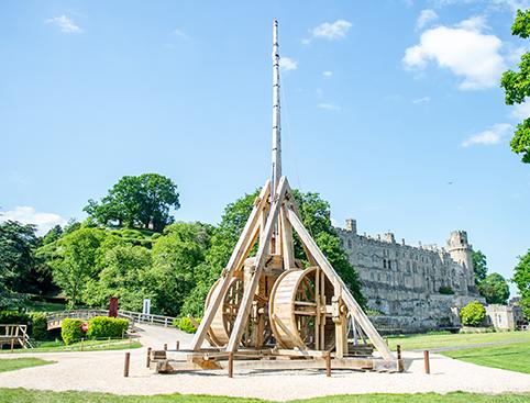 Warwick Castle Tickets | Wooden trebuchet with a medieval castle in the background.