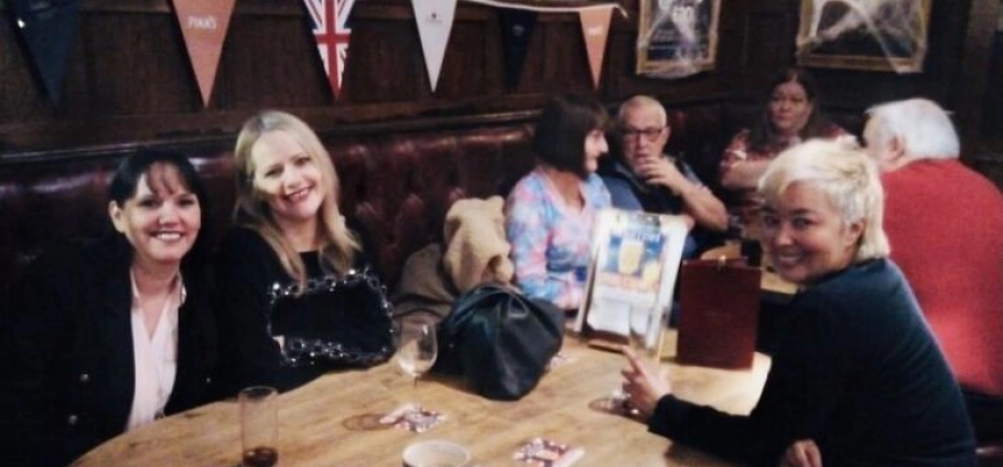 People sitting and chatting around a table in a pub with flag decorations on the wall.